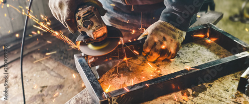 Schilderij op canvas Skilled worker using an angle grinder to cut and grind metal, generating bright sparks in a workshop environment, focusing on craftsmanship and industrial work