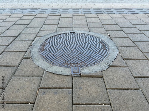Urban surface and infrastructure texture. Manhole lid on tile floor of train station platform, perspective view.
