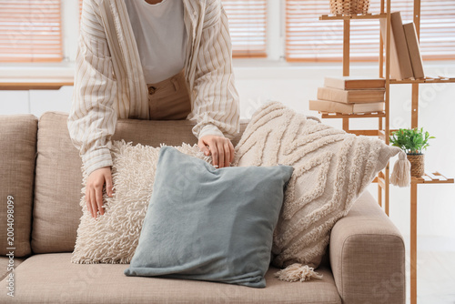 Photos Young woman fluffing pillows on cozy sofa in living room