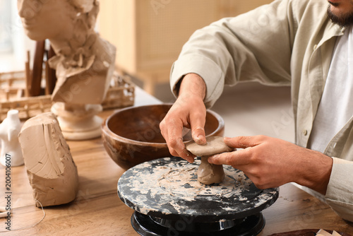 Fotografie Young male sculptor shaping clay figure on pottery wheel in workshop, closeup