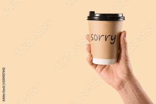 Foto Hand with paper cup of coffee with word SORRY on beige background