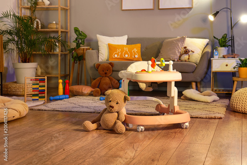 Baby walker with plush bear and toys in stylish living room at evening