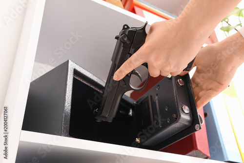 Quadro su tela Woman putting pistol into safe on shelf in office, closeup