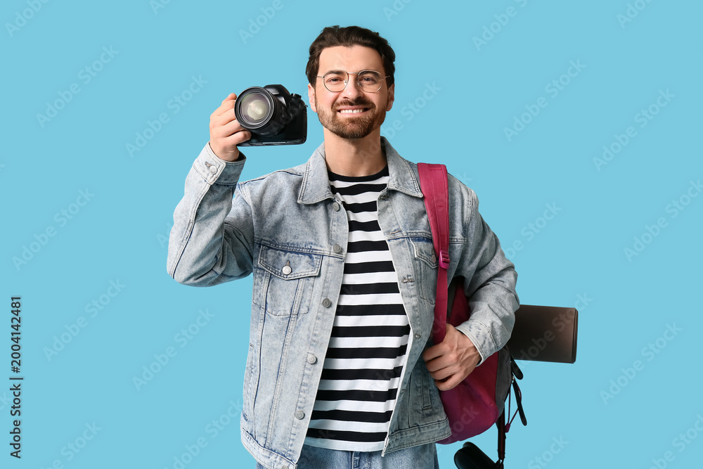 Naklejka premium Young male tourist with photo camera and backpack on blue background