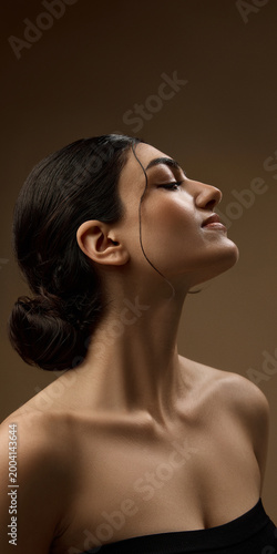 Fotografie Side profile of beauty model with sleek hair and glowing skin on brown background