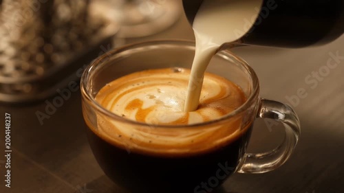 Espresso coffee with milk mixing creating creamy swirl in glass cup close up cinematic shot