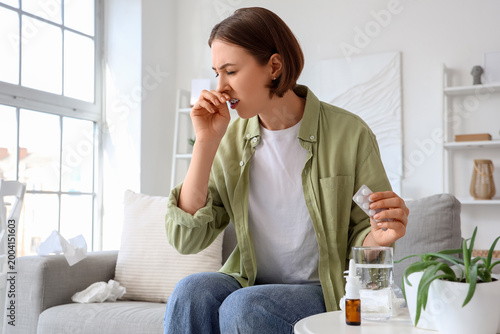 Billede på lærred Allergic young woman with pills sneezing at home