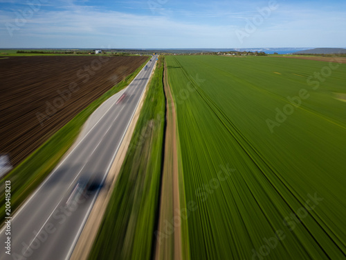 Fast motion blur aerial view of highway through green agricultural fields