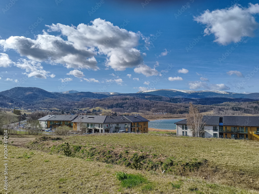 Fototapeta premium Landscape view of modern holiday houses near lake under blue sky with clouds. Concept of travel destination, eco tourism, peaceful retreat, nature and architecture.
