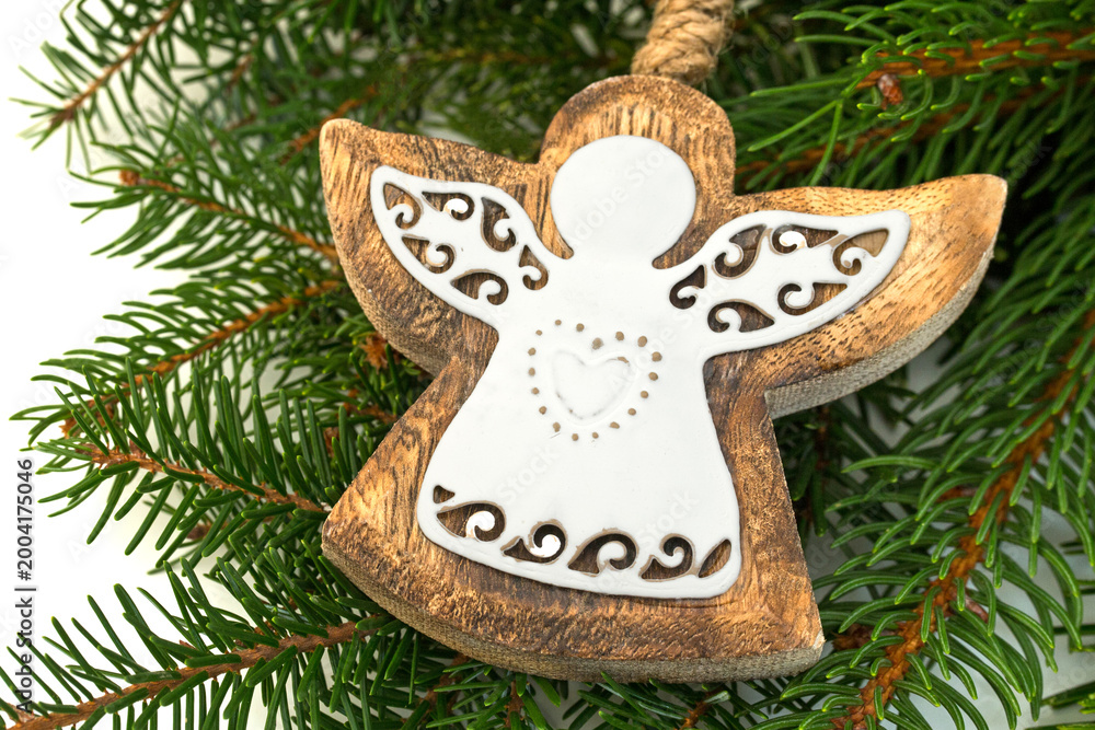 Fototapeta premium Wooden angel ornament hangs on green pine branches during winter holiday season