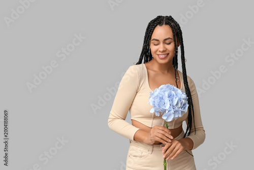 Beautiful young African-American woman with hydrangea flower on grey background