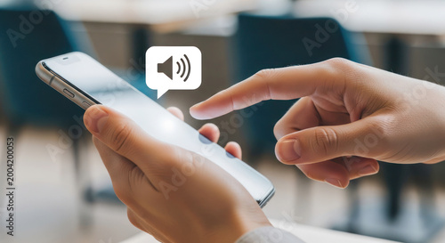 Close-up of hand tapping smartphone screen with sound icon, modern indoor setting with blurred background of chairs and tables
