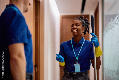 Happy professional janitors communicating while cleaning office building.