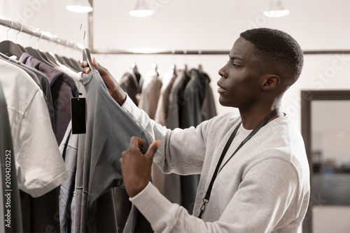 Quadro su tela young man browsing jackets on clothing rack in modern boutique store interior