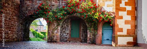 Photography Explore a cobblestone street with archways and blooming flowers in a village dur