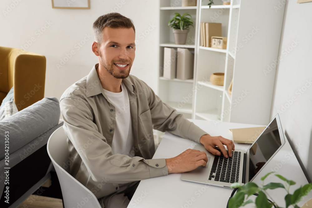 Naklejka premium Young bearded man using laptop on table at home