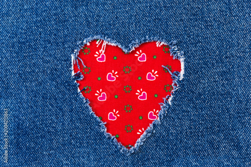 Foto Denim fabric with a heart-shaped hole revealing red patterned fabric underneath