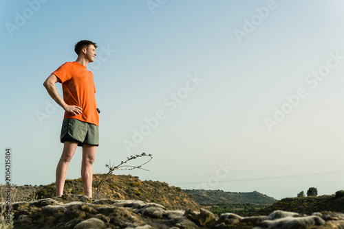 Valokuva Young runner standing on hill looking ahead at landscape