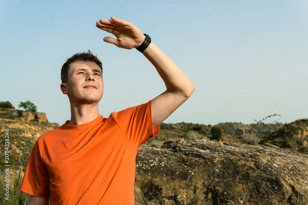 Naklejka premium Young man sheltering eyes from sun exploring nature