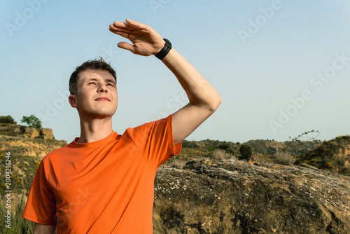 Young man sheltering eyes from sun exploring nature