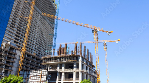 Fotografie Building cranes constructing a new modern skyscraper and developing urban infras
