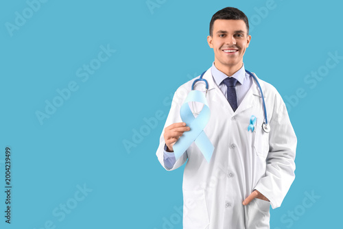 Male doctor with blue ribbon on color background. Prostate cancer awareness c...