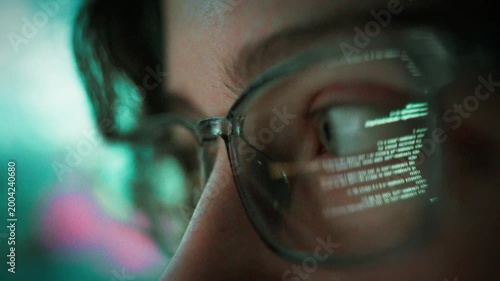 At night a young programmer sits before a glowing PC monitor, typing code while the screen's light reflects in her glasses, highlighting the focused atmosphere of a modern coding session