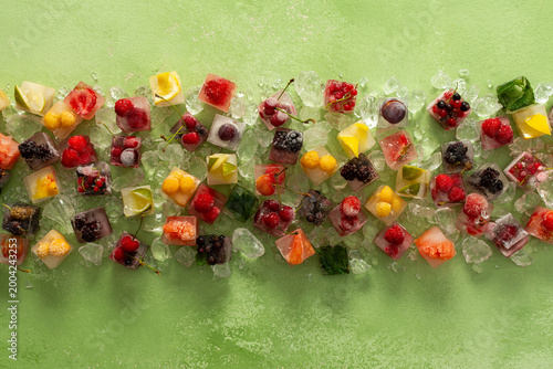 Green background with ice cubes with frozen berries and fruits and mint
