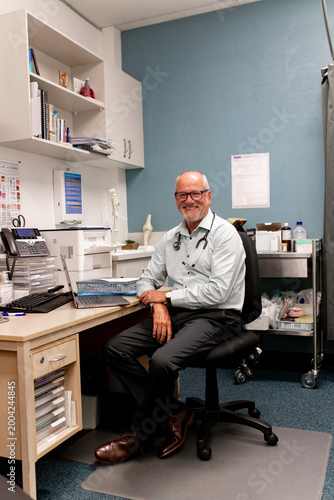 Portrait of a male doctor seated at desk with laptop and medical supplies