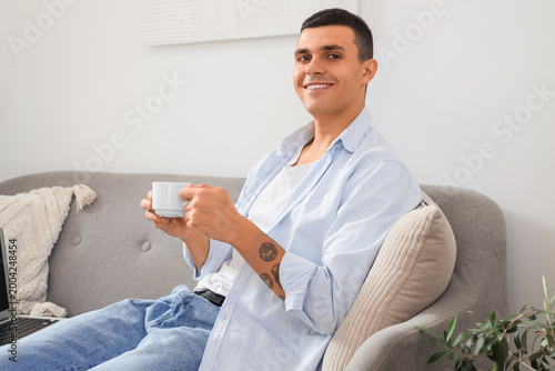 Handsome young man with cup of coffee resting on sofa in living room