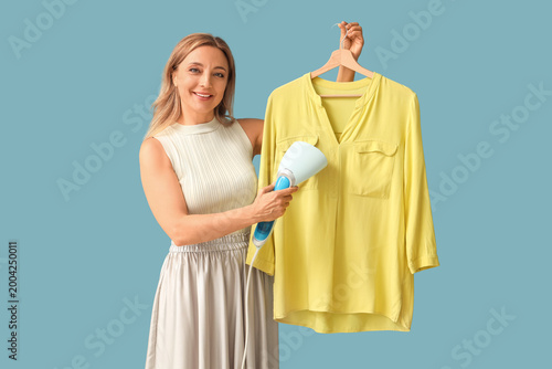 Quadro em tela Mature woman steaming shirt on blue background