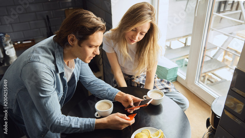 Billede på lærred Couple using phone and bank card for online order at kitchen table