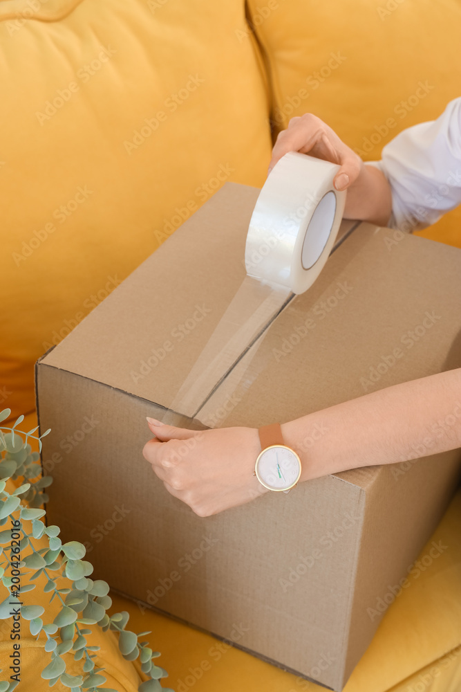 Fototapeta premium Woman taping cardboard box in office on moving day, closeup