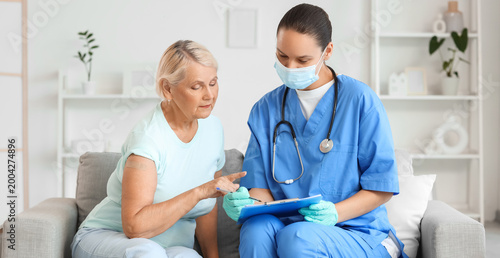 Senior woman with doctor sitting on sofa after vaccination at home