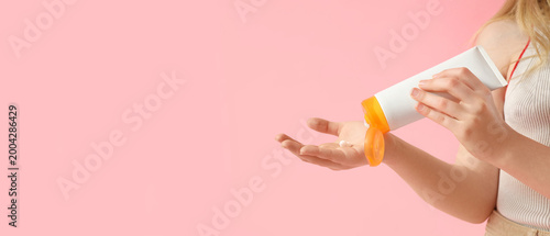 Quadro em tela Beautiful girl squeezing out sunscreen cream on pink background