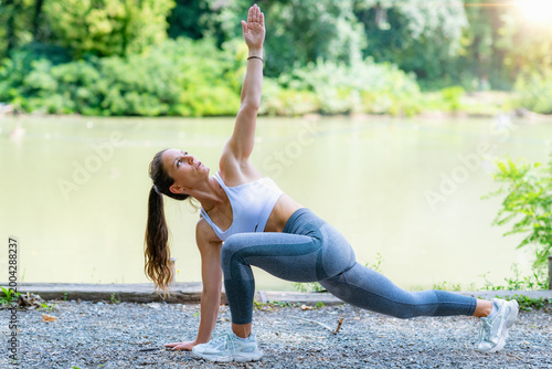 Obraz na płótnie Performing rotational lunge stretch with arm raised during outdoor workout, improving mobility, balance and flexibility