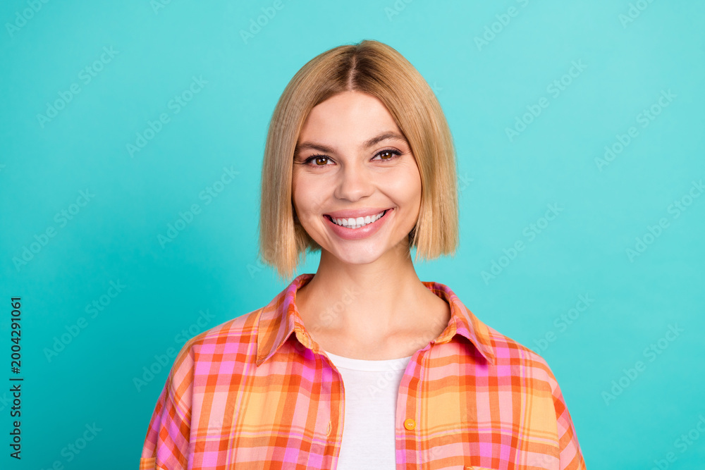 Fototapeta premium Smiling young woman portrait in a casual orange plaid shirt against a turquoise background conveying happiness, confidence, friendliness and approachable modern lifestyle