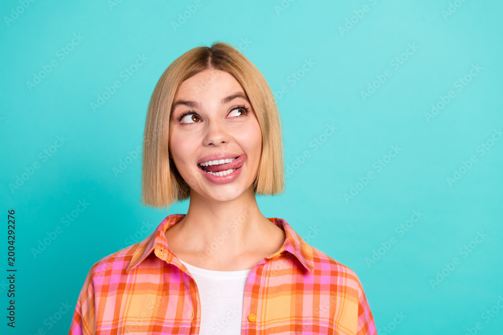 Fototapeta premium Playful young woman making a silly face and looking up against a turquoise background in a colorful plaid shirt portrait