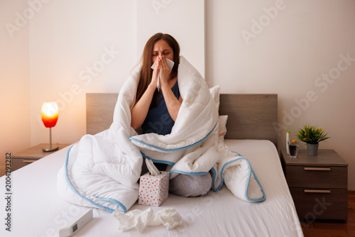 Woman having flu and fever blowing nose, coughing and sneezing while sick in bed