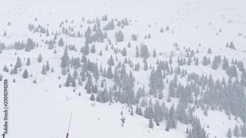 Ski lift rising above snowy slopes in Courchevel, France, surrounded by foggy alpine scenery during winter snowfall, with crowds of skiers descending the busy ski sl