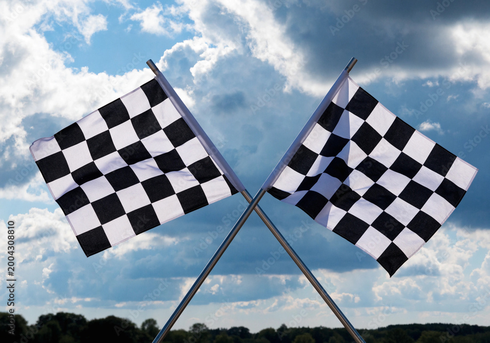 Fototapeta premium A black and white checkered flag flutters against a clear blue sky background to symbolize the finish of a high-speed Formula 1 racing competition and the success of the winner