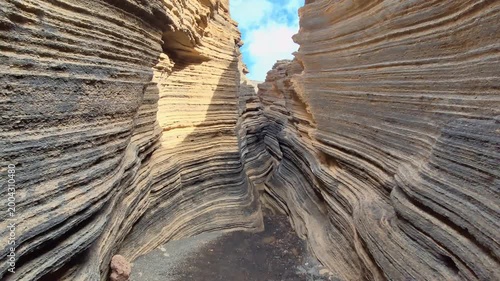 Camera hovering through lava fissures at Las Grietas on Montaña Blanca in Lanzarote, narrow volcanic cracks formed by eruptions, dramatic aerial perspective of rugged Canary Islands landscape.