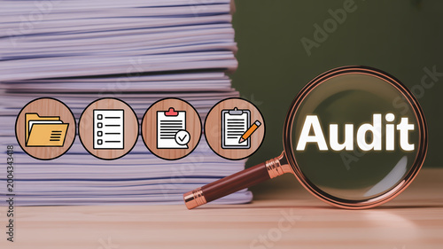 Magnifying glass over wooden blocks spelling out audit with coins and documents