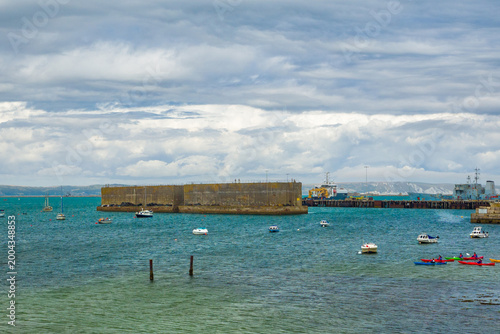 Coastal landscape of a harbor showing historical military structures, navy ships, and recreational kayaks (Portland, England, United Kingdom)