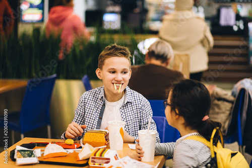 A thoughtful young boy and little girl sits at a fast food restaurant, eating burgers and drinking soda