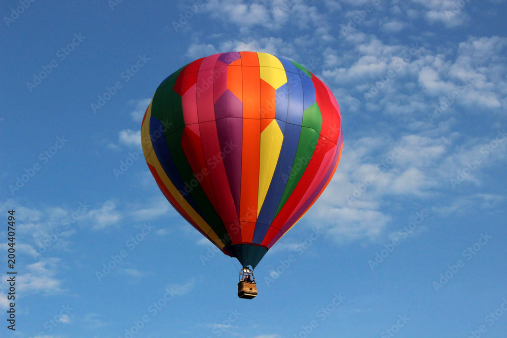 Naklejka premium Multicolored striped hot air balloon with geometric panels in blue sky