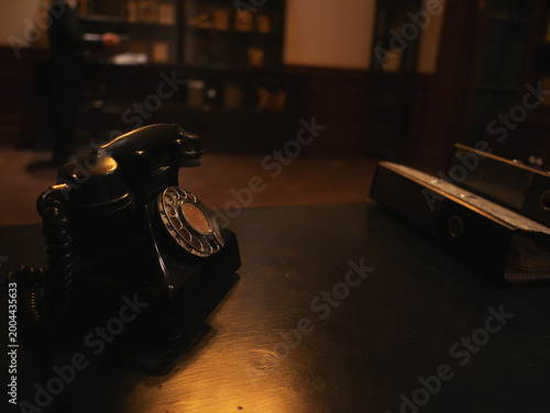 Vintage rotary telephone on wooden desk in dimly lit interior, nostalgic communication concept