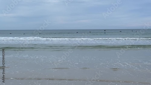 Soft waves move across a quiet shoreline beneath a wide cloudy sky. The peaceful coastal scene conveys relaxation and natural beauty.