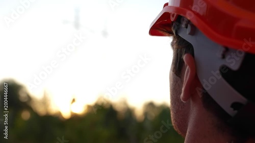 Young engineer standing outdoors while looking at the high voltage power lines. Back view. Energy industry concept. Real time