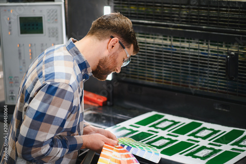 Printing factory worker checking color palette on press sheet